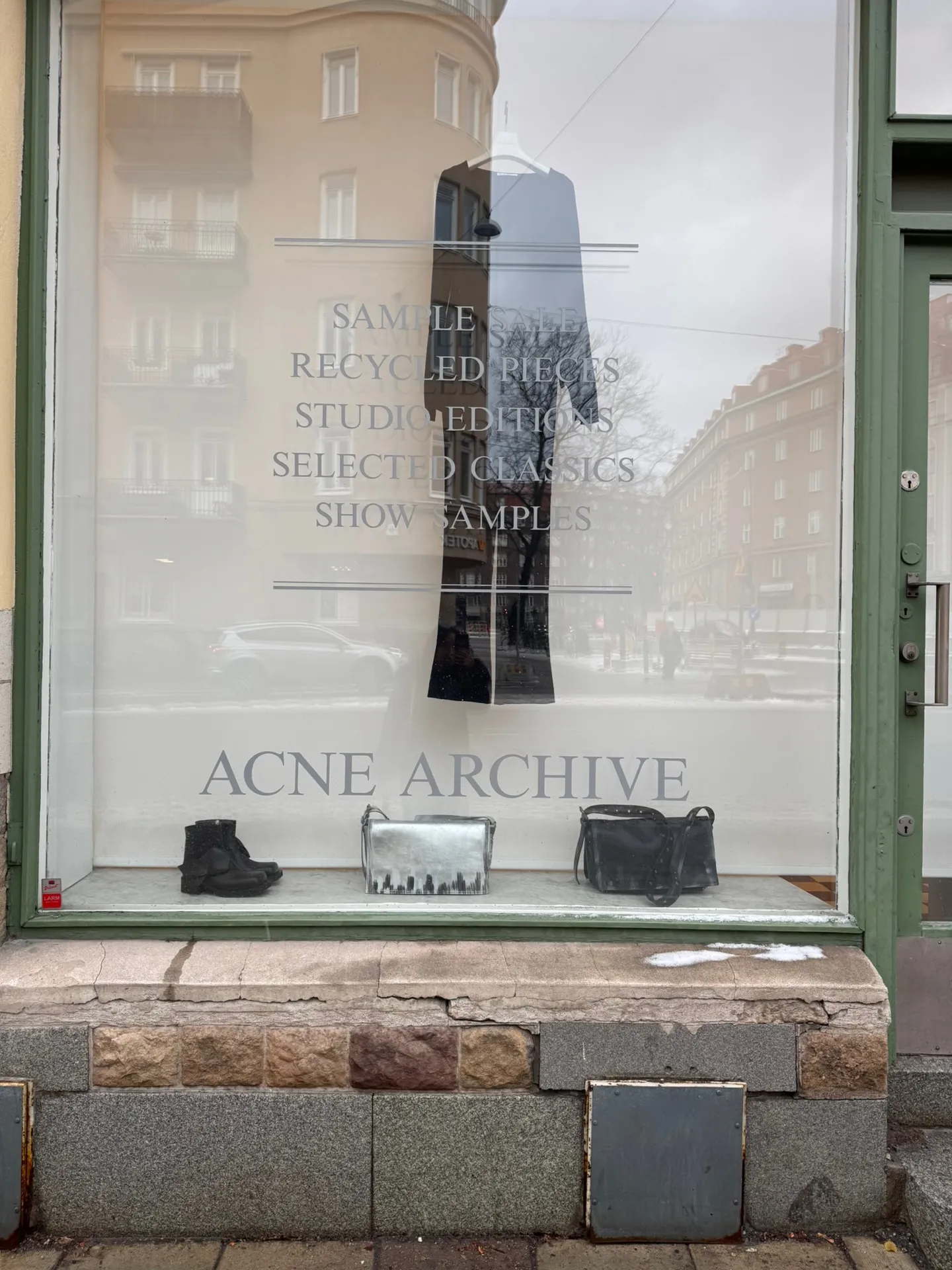 The Acne Archive storefront window in Stockholm, etched glass reading SAMPLE SALE, RECYCLED PIECES, STUDIO EDITIONS, SELECTED CLASSICS, SHOW SAMPLES above ACNE ARCHIVE, with boots and bags displayed on the sill.