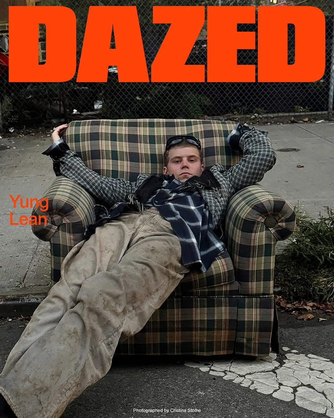 Yung Lean on the cover of Dazed's Winter 2025 Shadow Issue, sprawled in a discarded plaid armchair on a city street.