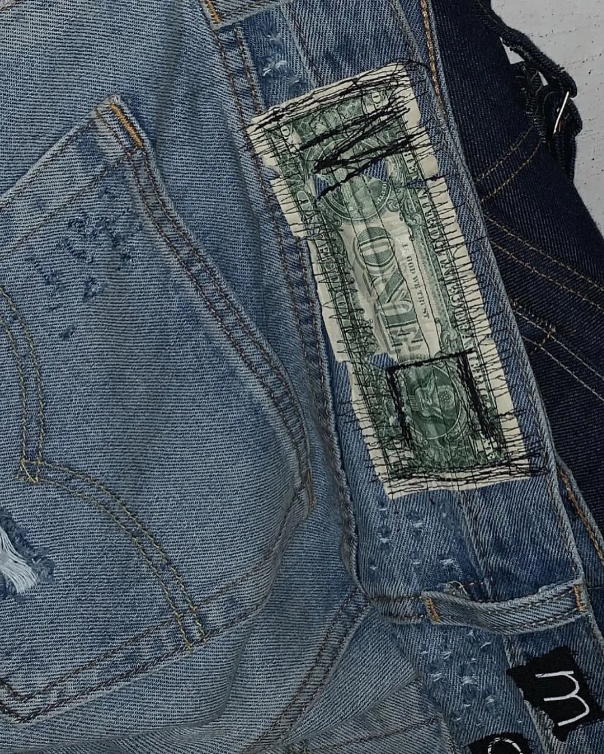 Close-up of jeans with a US one dollar bill stitched in place of a leather patch.