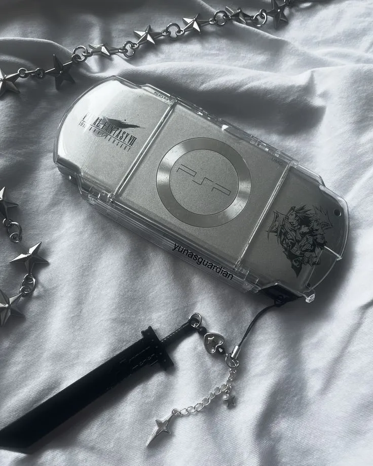 A clear PSP with Final Fantasy VII Advent Children artwork etched into the shell, a sword shaped keychain and a star link chain laid beside it.
