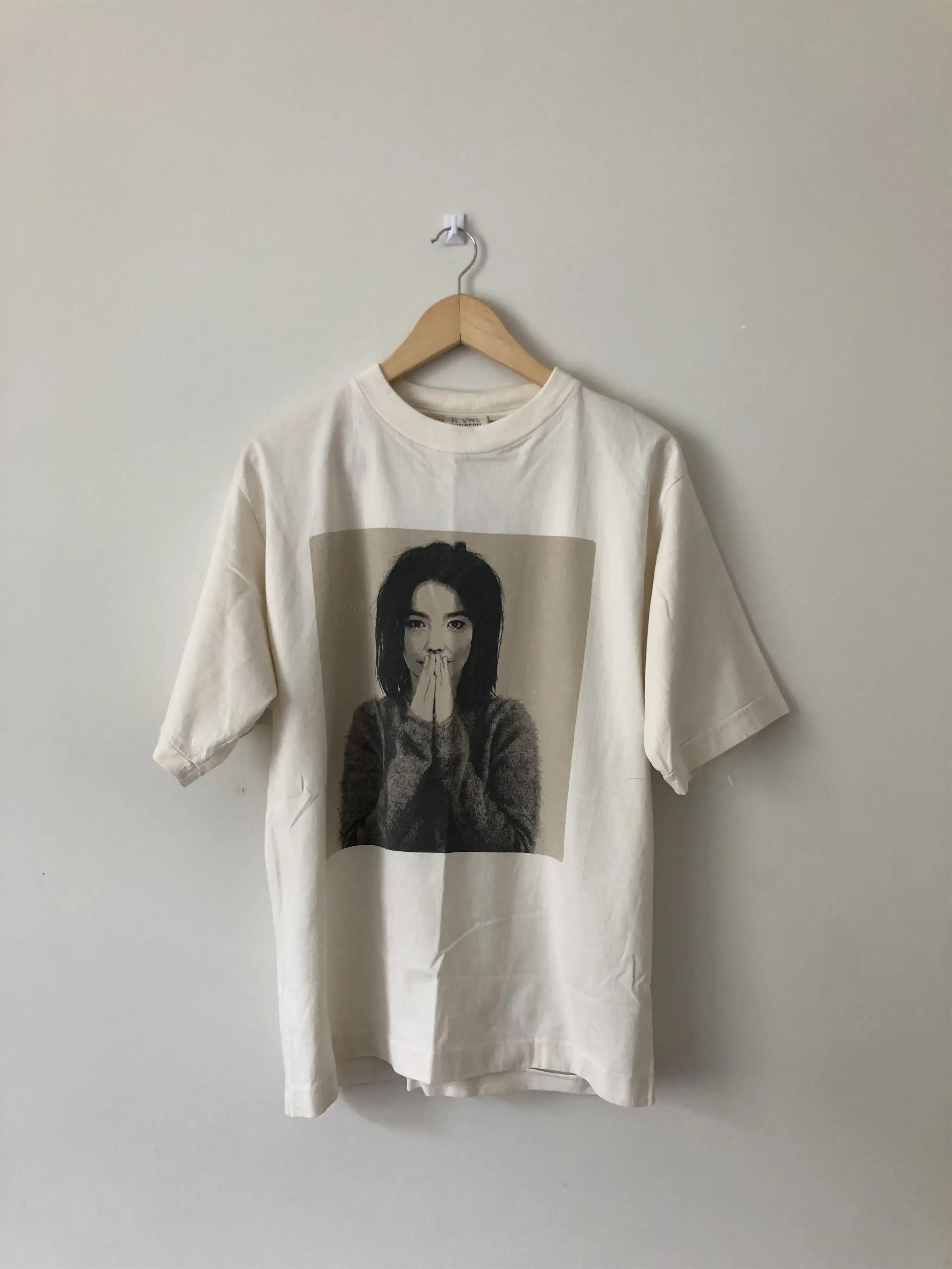 A cream Björk Debut t-shirt hanging in a parking garage, the printed portrait visible on the chest.