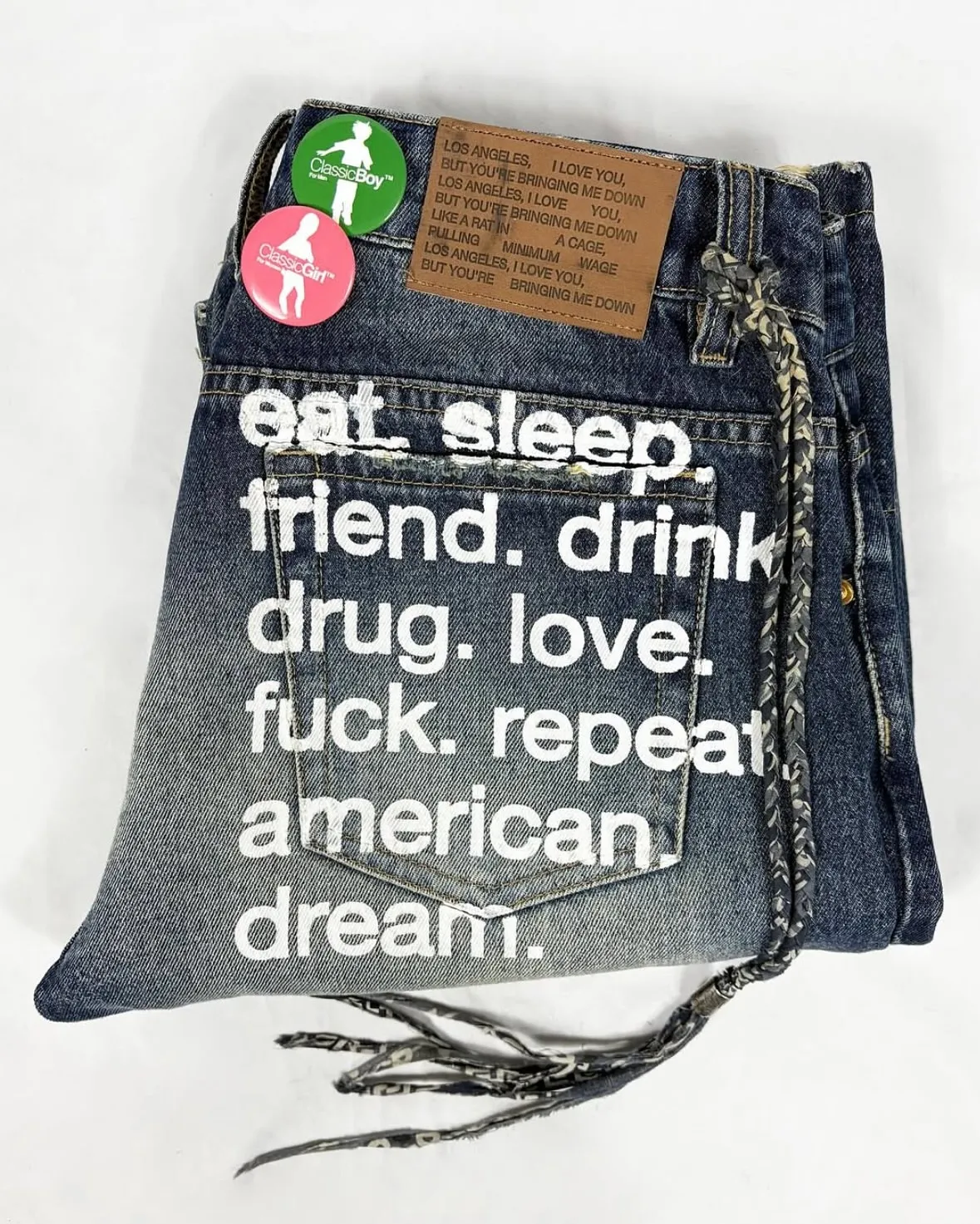 Distressed jeans with a leather patch stamped with a repeating line of text, and a back pocket printed with a list of words.