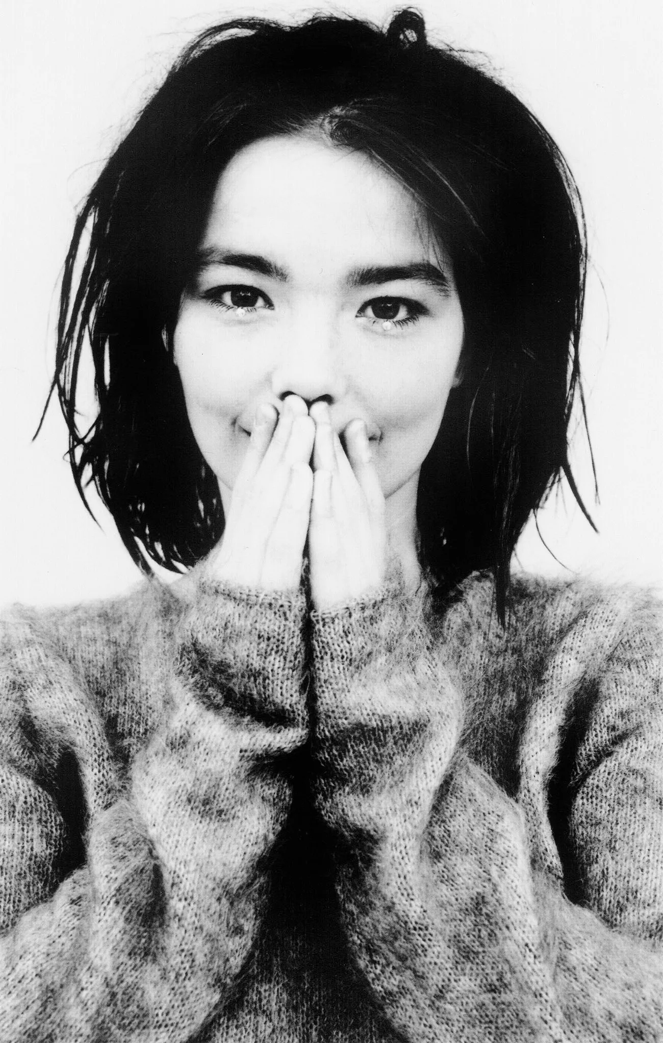 Black and white portrait of Björk with her hands pressed together in front of her mouth, wearing a mohair sweater, from the Debut album photoshoot.