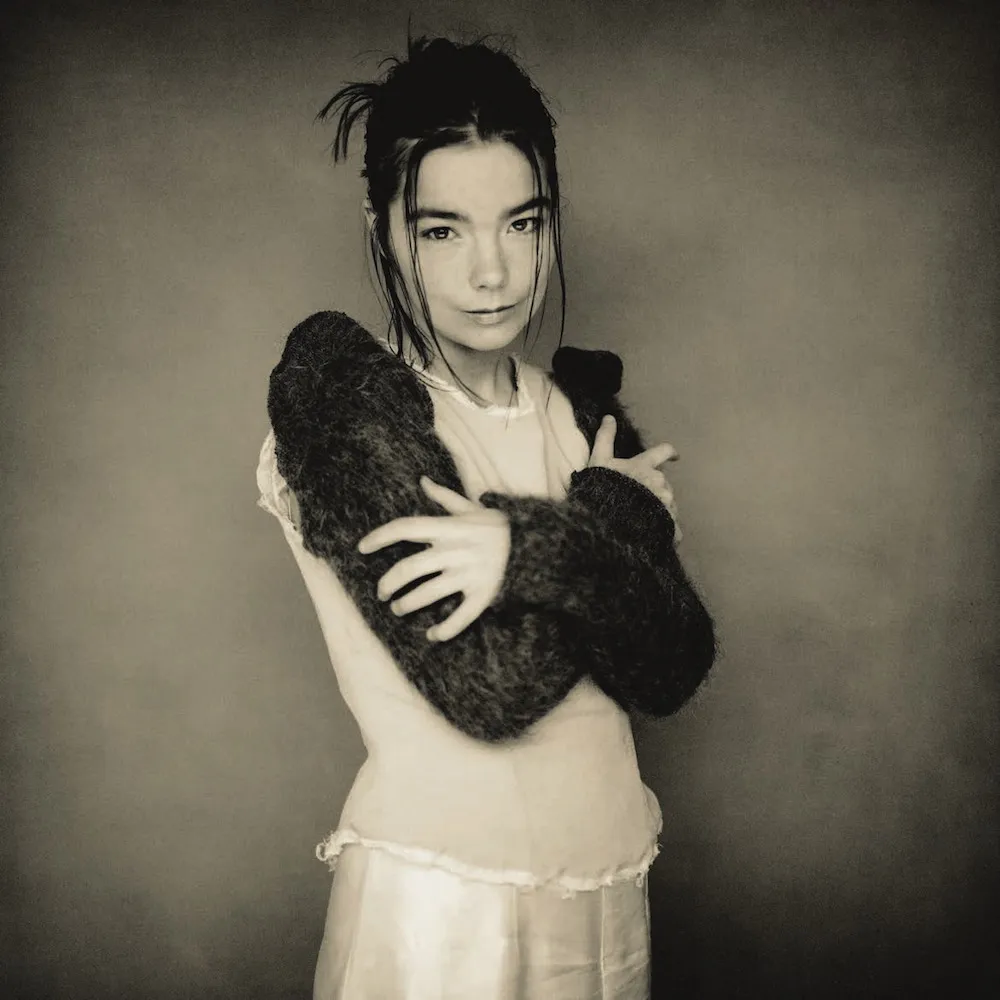 Black and white photograph of Björk kneeling with her chin resting on her hands, wearing lace-up boots, from the same 1993 session.