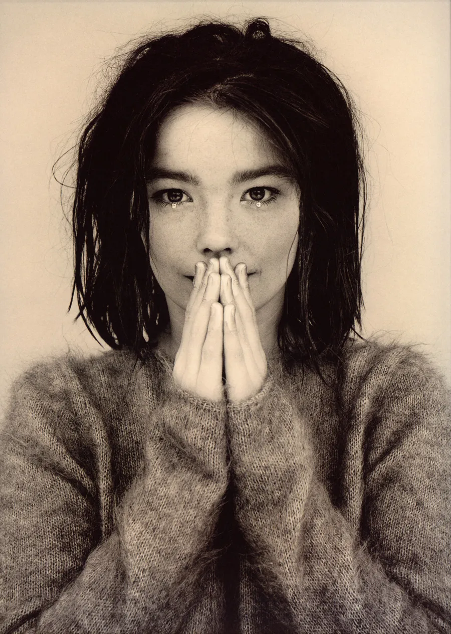 Sepia toned photograph of Björk with her hands pressed together in front of her mouth, from the same photoshoot as the Debut cover.