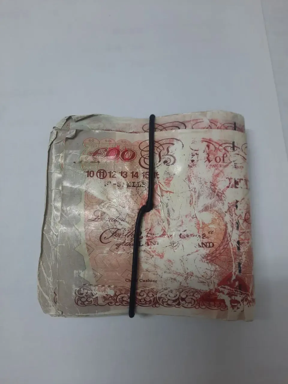 A worn leather wallet wrapped in a fake British 50 pound note, printed FAC-SIMILE, bound shut with a black elastic band.