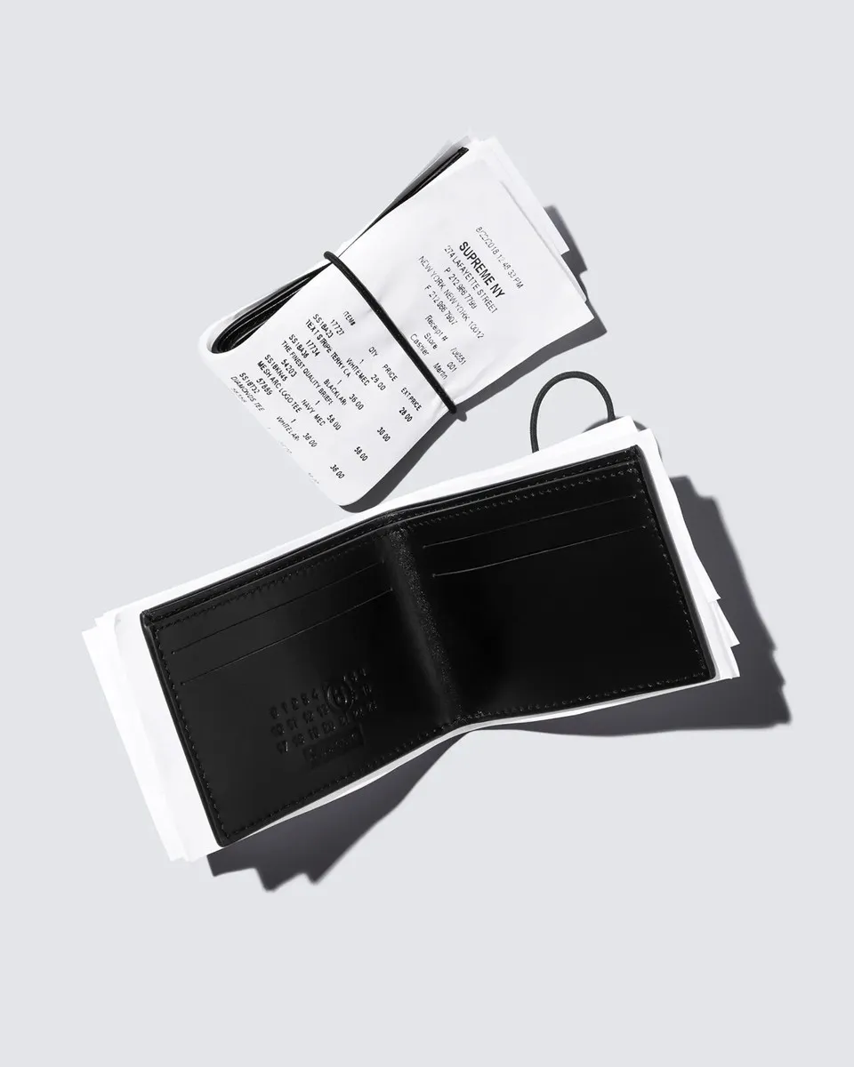 Two photos of the Supreme x MM6 Receipt Wallet: closed and rolled in a printed store receipt on the left, opened to show a black leather interior with card slots and an embossed circular logo on the right.