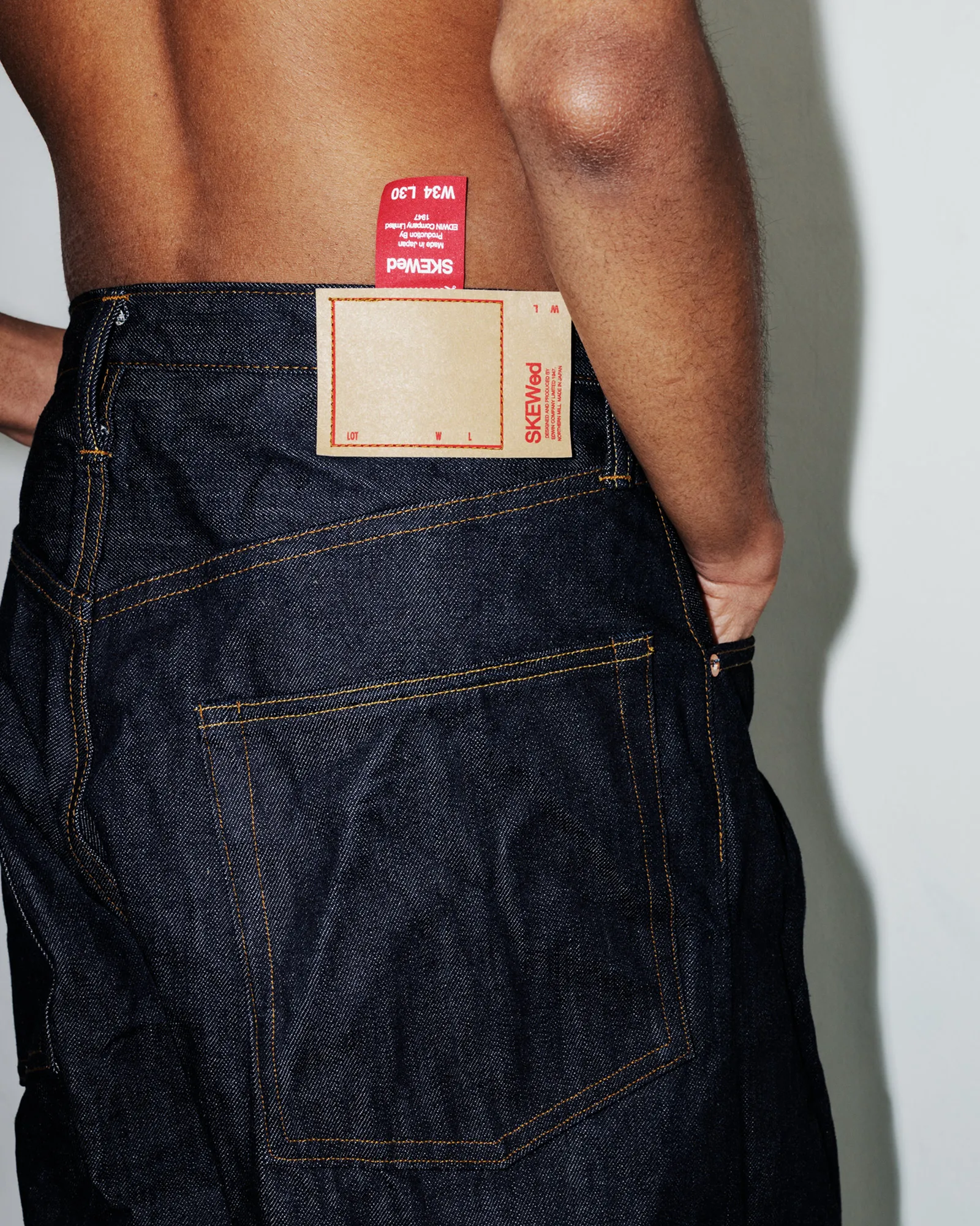 Raw indigo jeans photographed from behind, showing a blank tan jacron patch and a red mill tab.