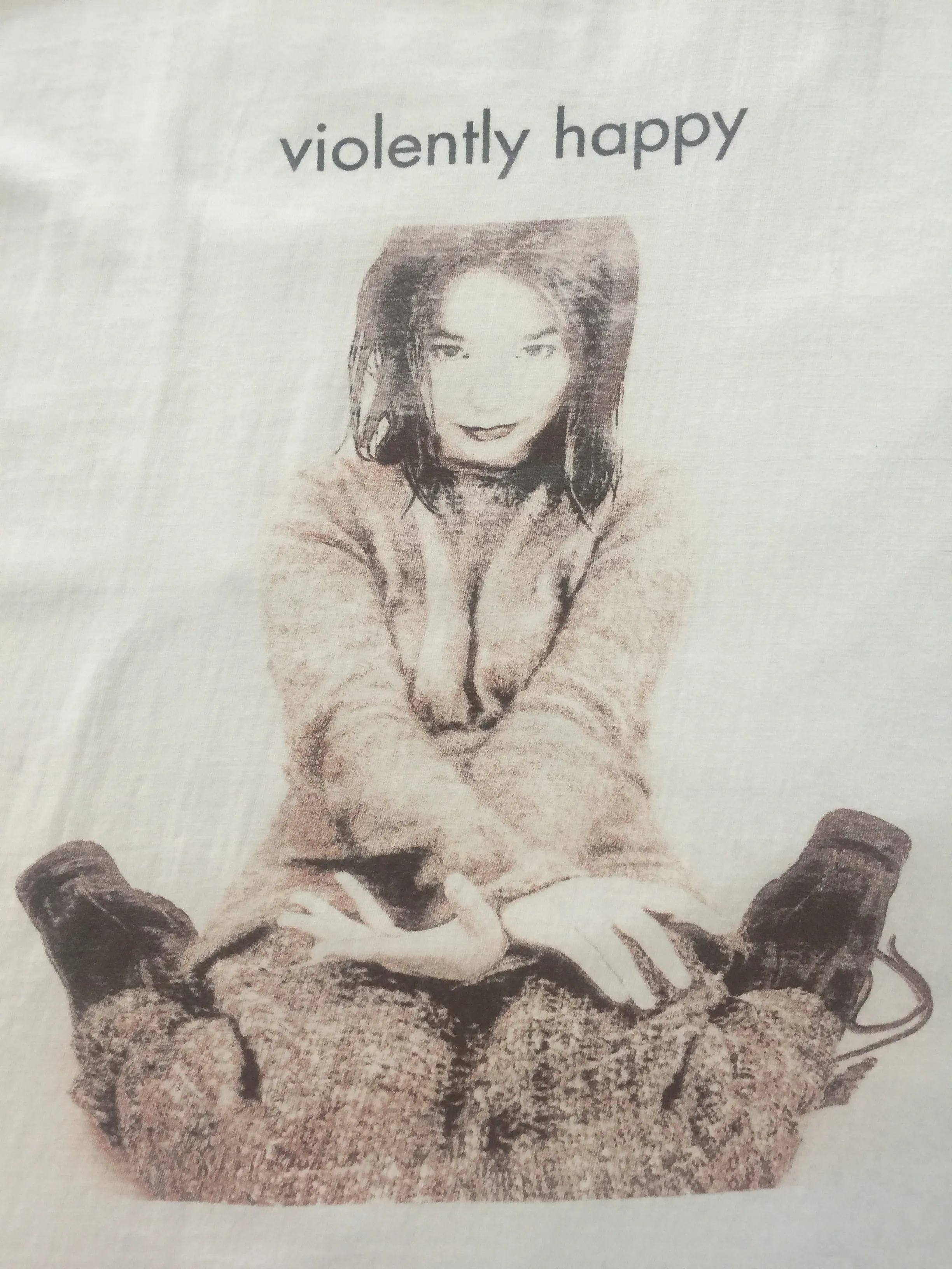A cream t-shirt printed with a Mondino photograph of Björk lying down, and the words violently happy underneath.